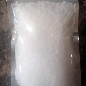 May include: A clear, resealable plastic pouch filled with small, opaque white wax pellets. The bag is rectangular and features a zip-lock closure at the top, containing a large quantity of uniform, round, solid white beads.