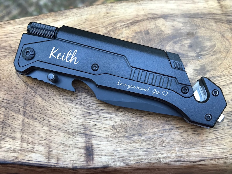 Puede incluir: Cuchillo multiusos de bolsillo negro con abridor de botellas, cortador de cinturones de seguridad y rompe cristales. El cuchillo est&aacute; grabado con el nombre "Keith" y el mensaje "Love you more! - Jen".