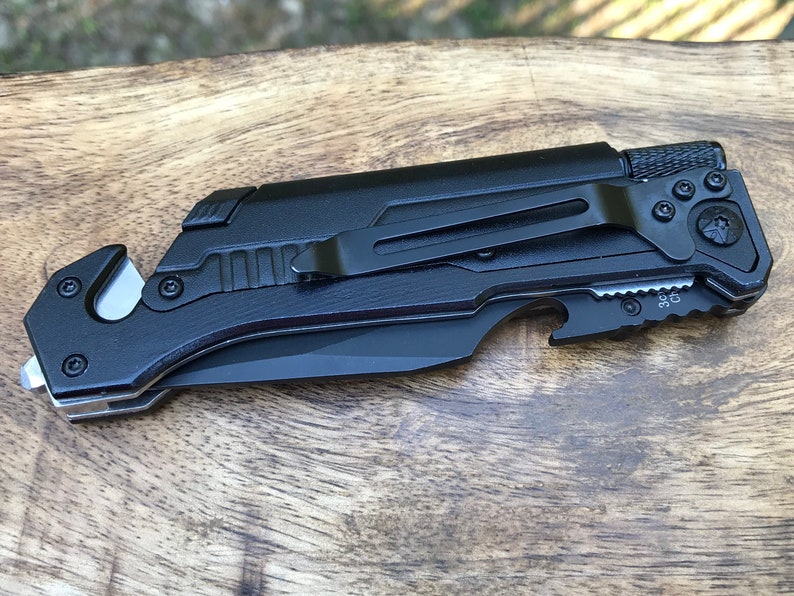 Puede incluir: Cuchillo plegable de bolsillo negro con una cuchilla de seguridad, abridor de botellas y clip para cintur&oacute;n. El cuchillo tiene un mango negro texturizado y una hoja negra.