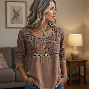 May include: A brown three-quarter sleeve top featuring an intricate floral embroidered yoke, a round neckline with decorative lattice trim, and a relaxed fit. The garment is paired with blue denim jeans and layered turquoise beaded necklaces.
