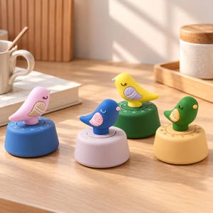 Puede incluir: Cuatro temporizadores de cocina con forma de pájaro, cada uno con una combinación de colores diferente: un pájaro rosa sobre base azul, uno azul sobre base lavanda, uno amarillo sobre base verde y uno verde sobre base amarilla.