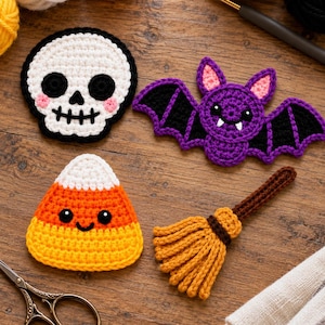 Puede incluir: Cuatro apliques de ganchillo con temática de Halloween que incluyen una calavera blanca con ojos negros, un murciélago morado con alas negras, un caramelo de maíz amarillo, naranja y blanco, y una escoba marrón y naranja sobre madera.