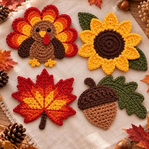 May include: Four crocheted appliques featuring autumn themes: a brown turkey with red, orange, and yellow tail feathers; a yellow sunflower with a brown center and green leaves; a red and orange maple leaf; and a brown acorn with a green oak leaf.