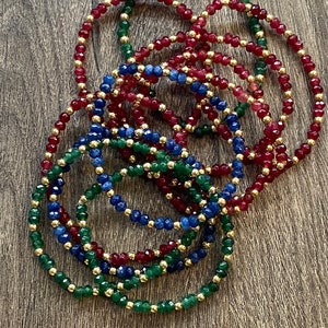 May include: A set of beaded bracelets in red, green, and blue colors. The bracelets are made with small, faceted beads and gold spacers.