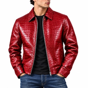 Könnte beinhalten: Eine leuchtend rote Jacke mit glänzender, geprägter Krokodilleder-Optik. Die Jacke hat einen klassischen Kragen, lange Ärmel und einen durchgehenden silberfarbenen Metallreißverschluss in der Mitte. Sie wird über einem schwarzen Shirt und blauen Jeans getragen.