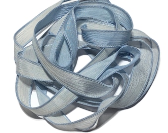 May include: A skein of light blue satin ribbon with a subtle textured pattern. The ribbon is approximately 1/2 inch wide and has a slightly frayed edge.