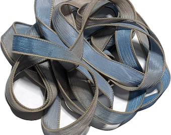 May include: A bundle of blue and gray satin ribbon with a subtle sheen. The ribbon is folded and twisted, creating a textured and layered effect.