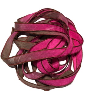 May include: A tangled bundle of decorative ribbon in shades of pink and brown. The ribbon has a textured appearance with a darker brown trim and stitching along the edges. The ribbon is likely used for crafts, gift wrapping, or other decorative purposes.