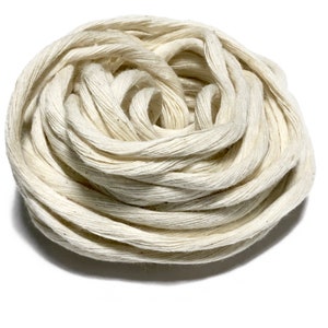 May include: A close-up of a large spool of natural white cotton twine. The twine is tightly wound and has a soft, natural texture.