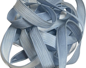 May include: A close-up of a light blue satin ribbon with a textured surface. The ribbon is folded and twisted, showing its delicate texture.