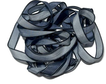 May include: A bundle of blue and gray satin ribbon with a black edge. The ribbon is twisted and folded, creating a textured look.