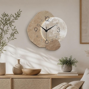 May include: A wall clock featuring a textured beige stone-like backing and a circular moon-patterned face. The clock has black hour and minute hands, with black numerals indicating the hours from 1 to 12 arranged around the central dial.