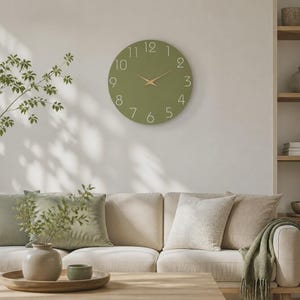 Peut inclure: Une horloge murale ronde au cadran vert olive mat, dotée de chiffres blancs fins de un à douze et d'aiguilles des heures et des minutes fines de couleur dorée. L'horloge présente un design circulaire épuré sans cadre, offrant une esthétique simple.