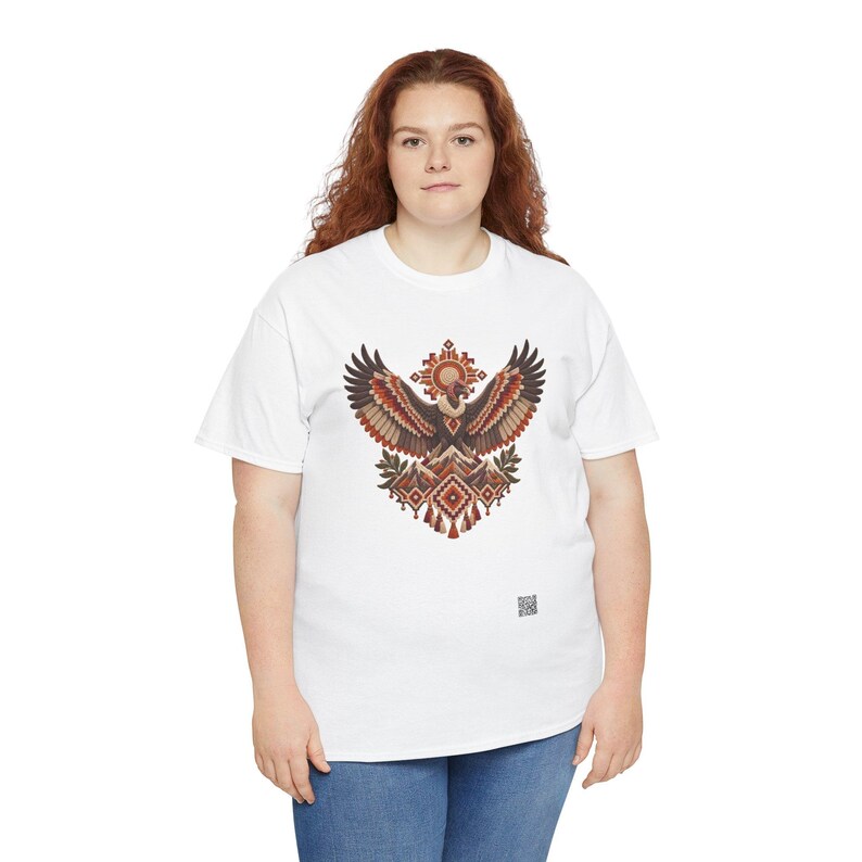 May include: A white short-sleeve t-shirt featuring a central graphic of a stylized eagle with wings spread wide. The design incorporates geometric patterns, mountain shapes, and a sun motif in shades of brown, orange, and cream.