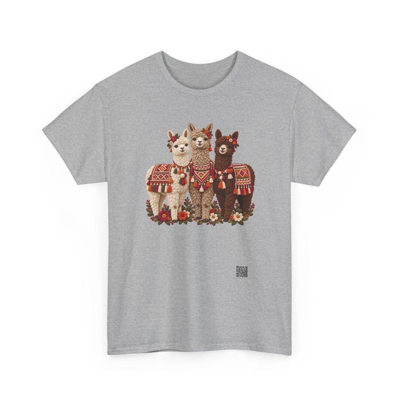 May include: A heather gray t-shirt featuring a graphic of three alpacas in white, tan, and dark brown. Each alpaca wears a colorful patterned blanket with tassels and floral headpieces. The alpacas stand among small flowers at the base.