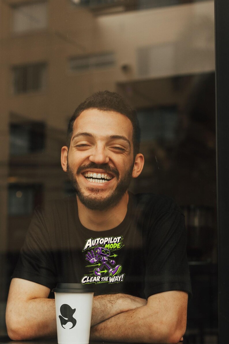 May include: A black t-shirt featuring a graphic of a purple robot with green accents. The text above the robot reads AUTOPILOT MODE and the text below reads CLEAR THE WAY! The design includes green arrows pointing in opposite directions.
