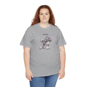 May include: A heather gray short-sleeve t-shirt featuring a graphic illustration of a curly-haired poodle wearing a purple bow on its head. The word Poodle is printed in black text above the dog illustration on the front of the shirt.