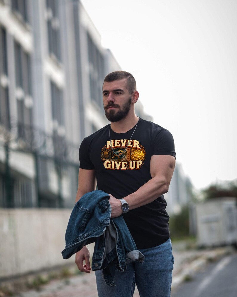 Puede incluir: Una camiseta negra de manga corta con un estampado gr&aacute;fico de un minero trabajando en una cueva y el texto NEVER GIVE UP en letras amarillas. El dise&ntilde;o incluye tonos naranjas y marrones con una escena de cristales brillantes.