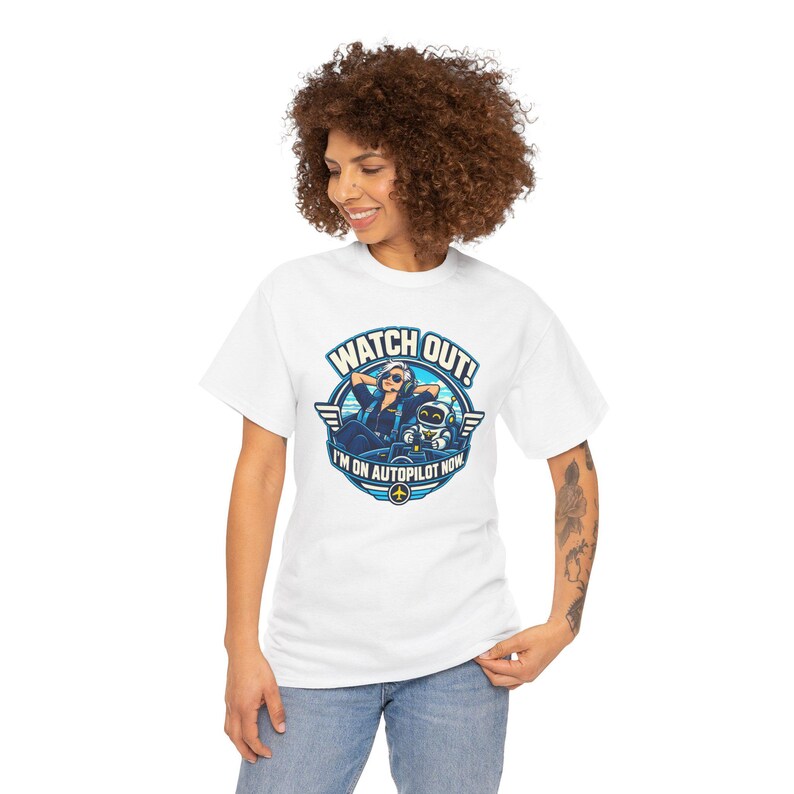 May include: A white short-sleeve t-shirt featuring a circular graphic of a pilot and a robot in a cockpit. The text reads WATCH OUT! I'M ON AUTOPILOT NOW. The design uses blue, white, and yellow colors with wings on the sides of the circle.