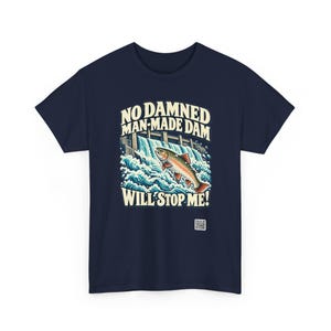Puede incluir: Una camiseta azul marino con un gr&aacute;fico de un pez saltando sobre una presa con salpicaduras de agua blanca. El texto dice: NO DAMNED MAN-MADE DAM WILL STOP ME! Un peque&ntilde;o c&oacute;digo QR cuadrado est&aacute; impreso en la parte inferior derecha.