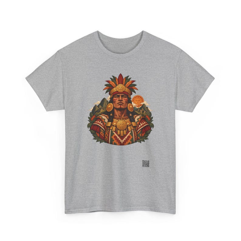 May include: A heather gray t-shirt featuring a central graphic of a person wearing an elaborate feathered headdress and gold jewelry. The design includes mountain silhouettes, a sun, and geometric patterns in red, gold, and green.