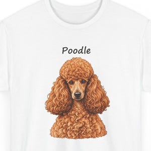 May include: A white t-shirt featuring a detailed illustration of a brown poodle with curly fur. The word Poodle is printed in black text above the dog's head. The design is centered on the front of the shirt, showcasing the dog's face.