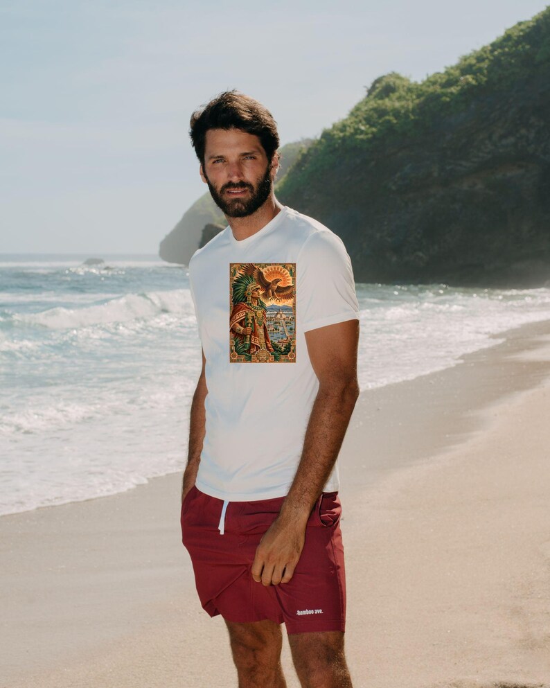 Pu&ograve; includere: Una t-shirt bianca a maniche corte con una stampa grafica rettangolare raffigurante un guerriero azteco con copricapo di piume e un'aquila, abbinata a pantaloncini sportivi bordeaux con coulisse bianca e piccolo testo bianco sulla gamba.