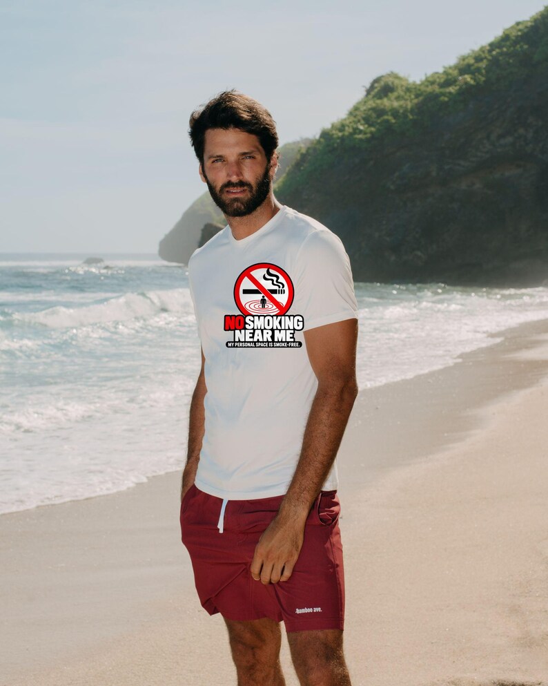 May include: A white short-sleeved t-shirt featuring a red circular no-smoking symbol with a cigarette graphic and the text NO SMOKING NEAR ME MY PERSONAL SPACE IS SMOKE-FREE, paired with maroon shorts featuring a white drawstring.