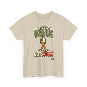 Op de afbeelding: Een beige t-shirt met een afbeelding van een lopend persoon. De tekst luidt I PREFER TO WALK NOT WORK, waarbij het woord WORK is doorgehaald met een horizontale lijn. De persoon draagt een groen overhemd, wit shirt en een bruine broek.