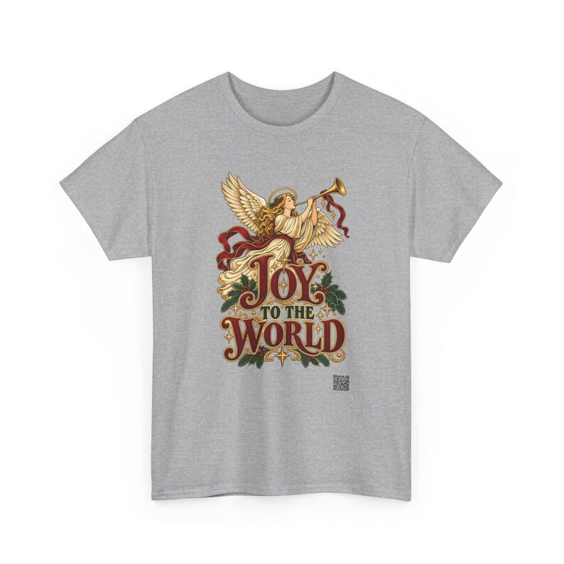 May include: A heather gray t-shirt featuring a graphic of an angel with large wings playing a golden trumpet. Below the angel, the text reads JOY TO THE WORLD in a decorative red font, accented with green holly leaves and small gold stars.