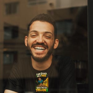May include: A black t-shirt featuring a graphic of a person partially transformed into a tree, with the text "I AM STUCK AS A TREE WHILE THEY GET TRILLIONS" in yellow and white lettering, positioned above a white cup with a black logo.