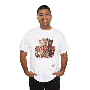 May include: A white short-sleeved t-shirt featuring a central graphic of three llamas standing together. The llamas are adorned with colorful patterned blankets, tassels, and floral headpieces in shades of red, orange, and green.
