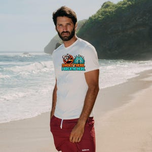May include: A white short-sleeved t-shirt featuring a graphic of a no-smoking symbol next to a pair of blue lungs, with the text "SMOKE THERE, I BREATHE HERE" printed in orange and blue, paired with maroon athletic shorts.