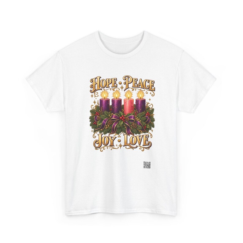 May include: A white t-shirt featuring a graphic of an Advent wreath with four lit candles in purple and pink, surrounded by evergreen branches and ribbons. The text HOPE PEACE is printed above the candles, and JOY LOVE is printed below in gold.