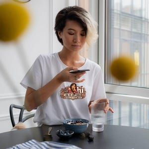 May include: A white short-sleeved t-shirt featuring a graphic print on the chest. The design includes an illustration of a person with long hair, the text "ai hi" and "ASK ME ANYTHING" in a decorative frame with small icons below the text.