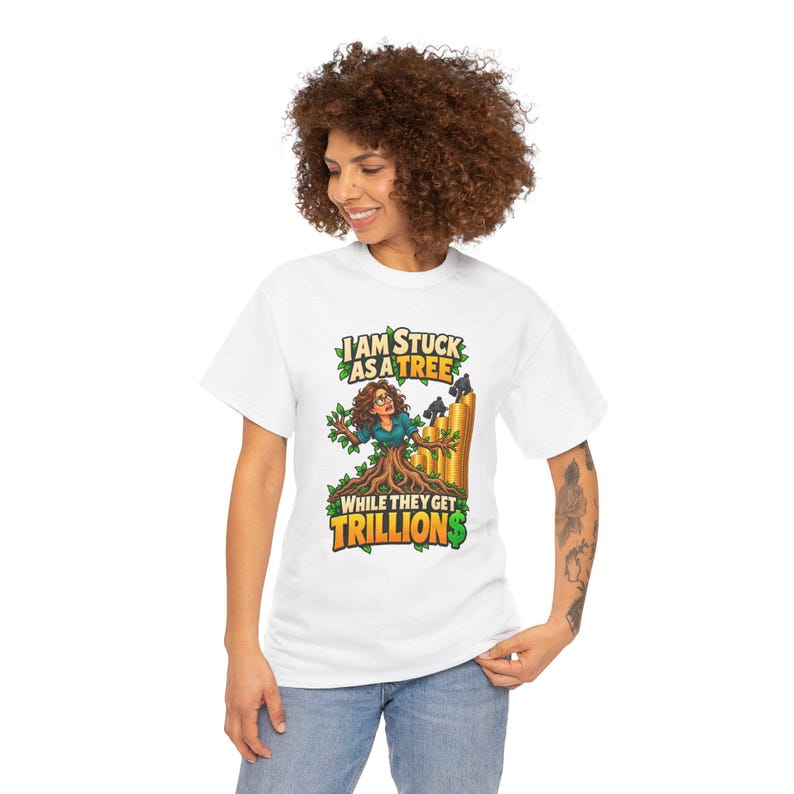 May include: A white t-shirt featuring a graphic of a person with brown hair emerging from a tree trunk. The text reads I AM STUCK AS A TREE WHILE THEY GET TRILLION$. The design includes green leaves and a stack of gold coins with small figures.