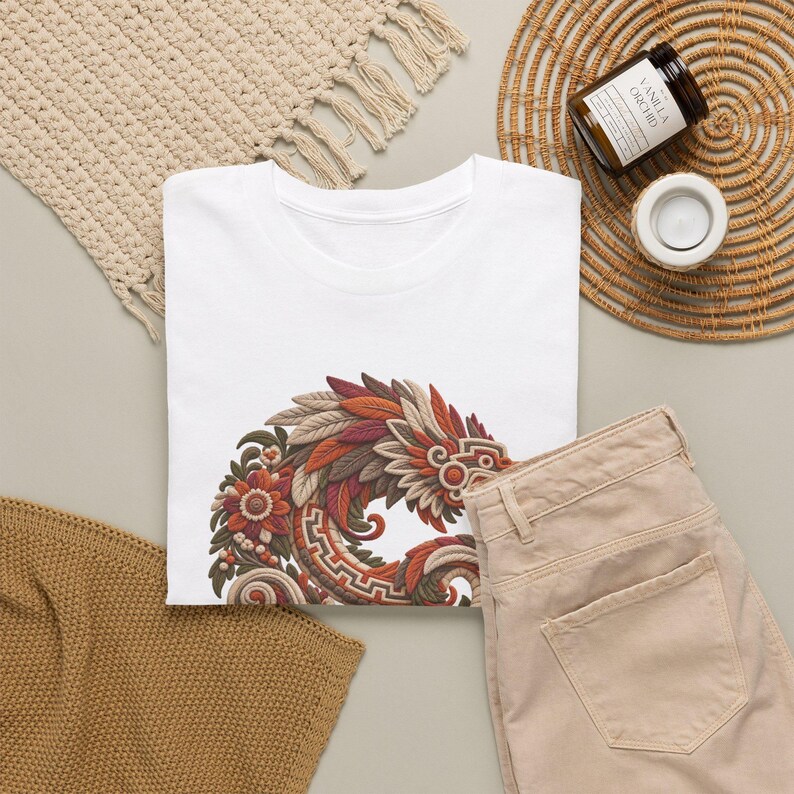 Puede incluir: Una camiseta blanca con un dise&ntilde;o gr&aacute;fico circular compuesto por plumas superpuestas, elementos florales y patrones geom&eacute;tricos en tonos &oacute;xido, naranja, marr&oacute;n y crema. El dise&ntilde;o est&aacute; situado en la parte inferior central de la camiseta.