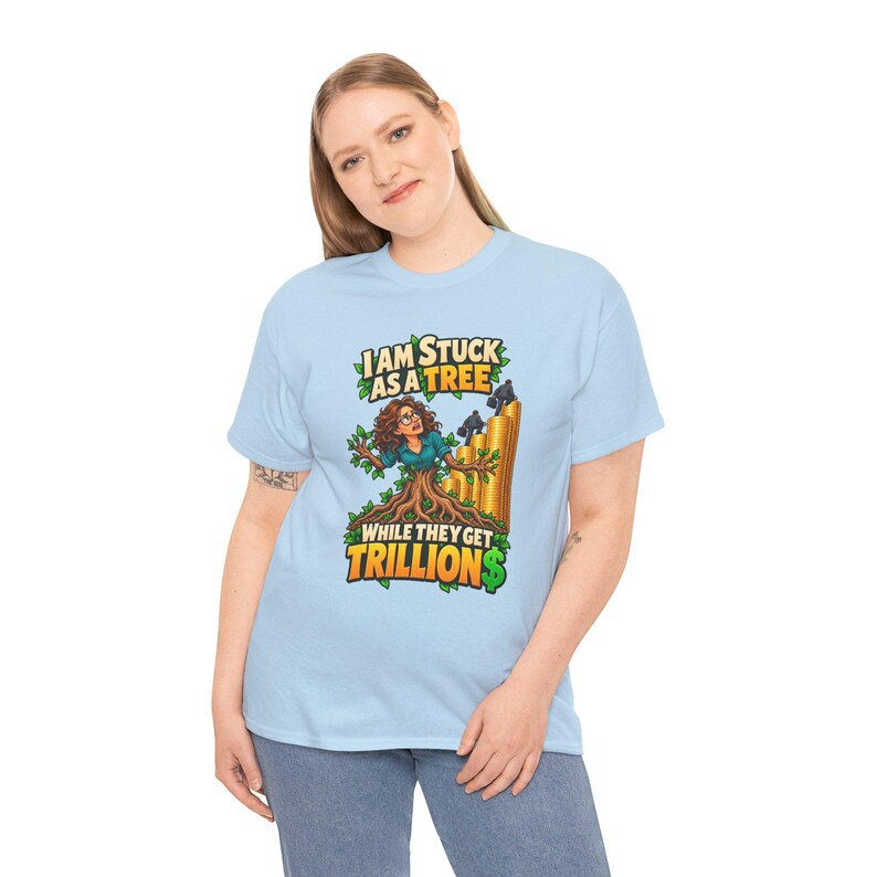 May include: A light blue t-shirt featuring a graphic of a person with tree branches for arms, stuck in a tree trunk, with figures climbing a stack of gold coins. The text reads: I AM STUCK AS A TREE WHILE THEY GET TRILLIONS.