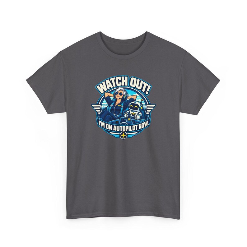 May include: A dark gray t-shirt featuring a circular graphic of a pilot and a small robot in a cockpit. The text reads WATCH OUT! I'M ON AUTOPILOT NOW. The design includes blue and white colors, wings, and a small yellow airplane icon.