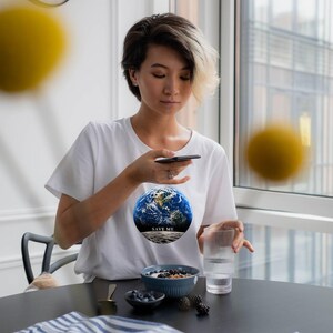 May include: A white short-sleeved t-shirt featuring a circular graphic of the Earth above a crescent moon with the text "SAVE ME" printed in black. The design is centered on the chest of the garment, which has a classic crew neckline.