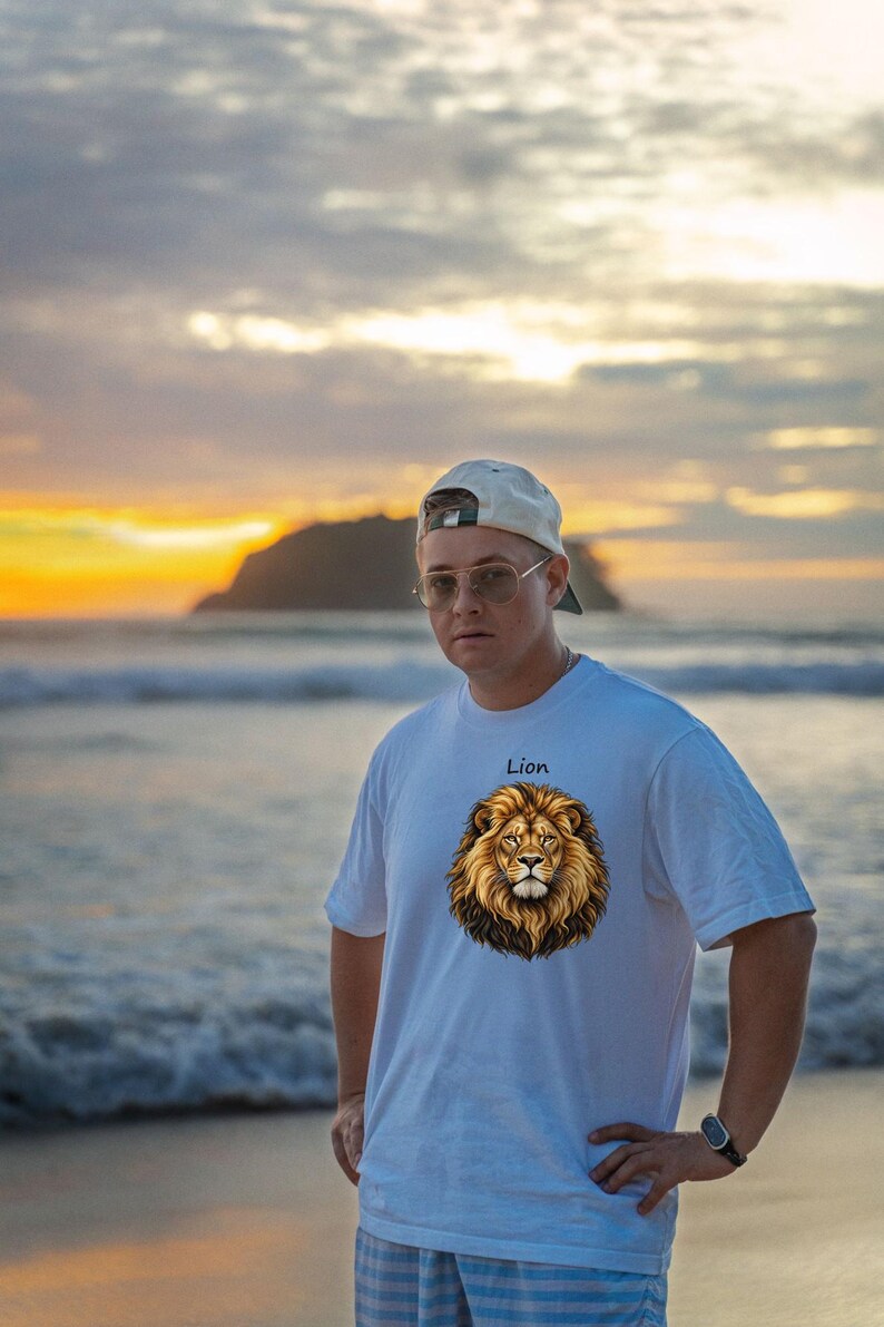 May include: A white short-sleeved t-shirt featuring a graphic print of a lion's head in the center of the chest with the word Lion printed in black text above the lion illustration. The shirt has a crew neckline and a standard fit.