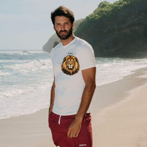 May include: A white short-sleeved t-shirt featuring a graphic of a lion's head on the chest with the text "Lion" above it, paired with maroon athletic shorts that have a white drawstring and a small white logo on the lower left leg.