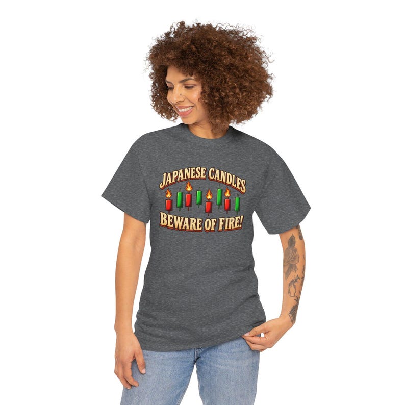 May include: A dark heather grey short-sleeve t-shirt featuring a graphic of red and green Japanese candlestick chart bars with flames on top. The text reads "JAPANESE CANDLES" above the graphic and "BEWARE OF FIRE!" below it.
