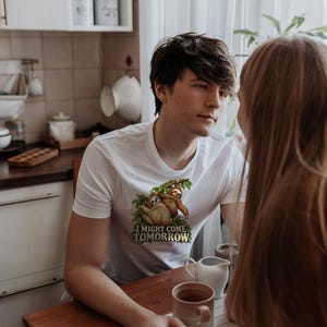 Pode incluir: Uma t-shirt branca de manga curta com uma impress&atilde;o gr&aacute;fica de duas pregui&ccedil;as castanhas penduradas em folhas verdes. Abaixo das pregui&ccedil;as, o texto I MIGHT COME TOMORROW est&aacute; escrito numa fonte a negrito verde-escura.