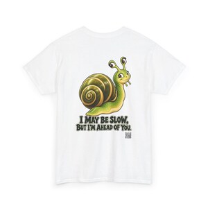 May include: A white t-shirt featuring a graphic of a green snail with a brown shell. Below the snail, the text reads, "I MAY BE SLOW, BUT I'M AHEAD OF YOU." A small QR code is printed in the bottom right corner of the graphic design.