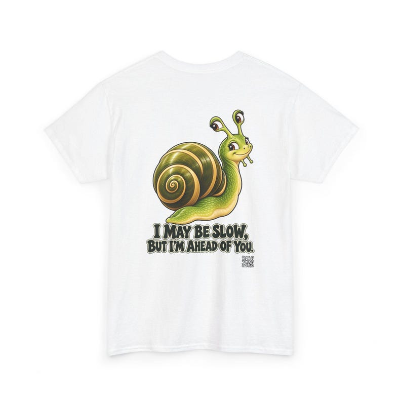 May include: A white t-shirt featuring a graphic of a green snail with a brown shell. Below the snail, the text reads, "I MAY BE SLOW, BUT I'M AHEAD OF YOU." A small QR code is printed in the bottom right corner of the graphic design.