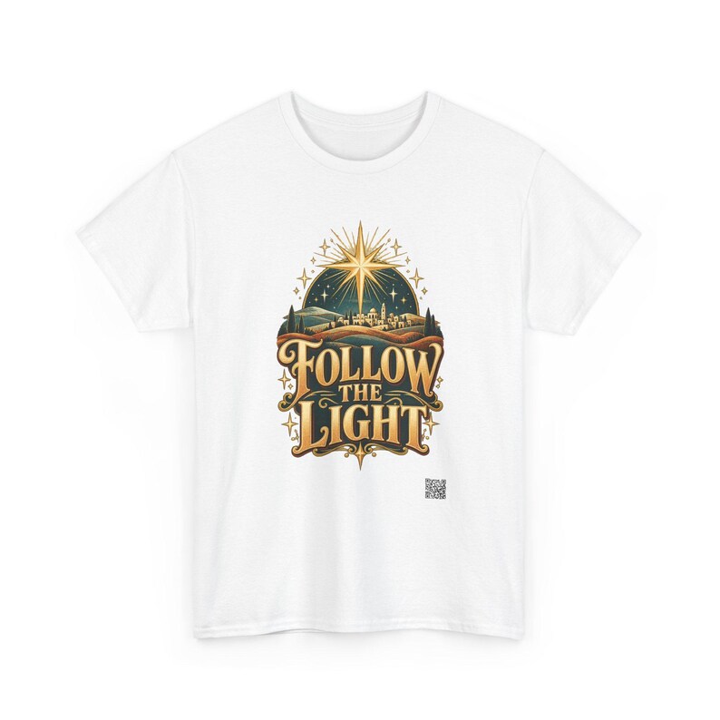 May include: A white short-sleeve t-shirt featuring a central graphic of a glowing star above a landscape with the text FOLLOW THE LIGHT in gold lettering. The design includes a dark blue night sky, rolling hills, and a small QR code below.