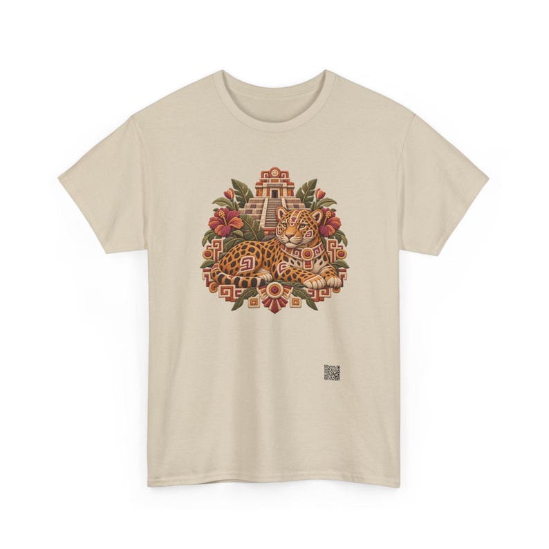 May include: A beige short-sleeve t-shirt featuring a central graphic of a spotted jaguar resting in front of a stepped pyramid. The design includes red hibiscus flowers, green leaves, and geometric patterns in shades of orange and brown.