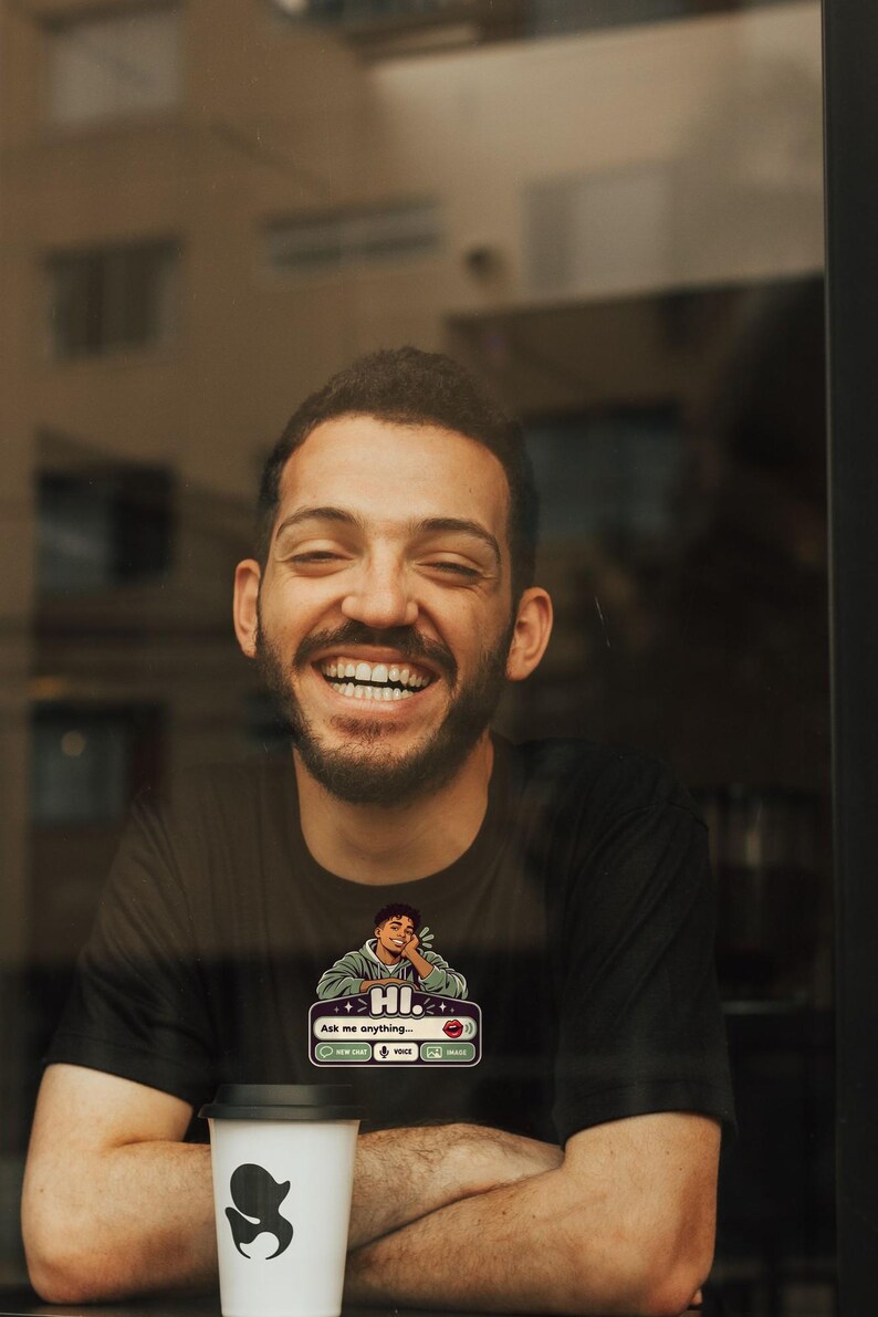 May include: A black t-shirt featuring a graphic print of a person resting their chin on their hand above a chat interface box that reads HI. Ask me anything... with icons for new chat, voice, and image, paired with a white coffee cup.