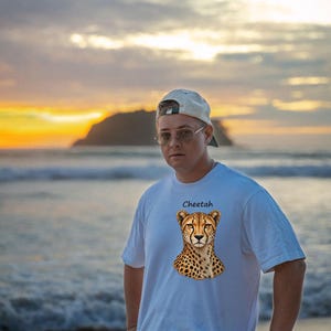 Op de afbeelding: Een wit T-shirt met korte mouwen en een grafische print van de kop en schouders van een jachtluipaard in het midden van de borst, met het woord Cheetah in zwarte letters boven de illustratie.